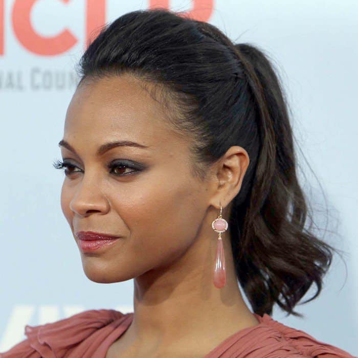 Zoe Saldaña's hair was styled in a voluminous bouffant ponytail, and her makeup included smoky eyes and a striking fuchsia-pink lip color, perfectly rounding off her sophisticated and stylish look