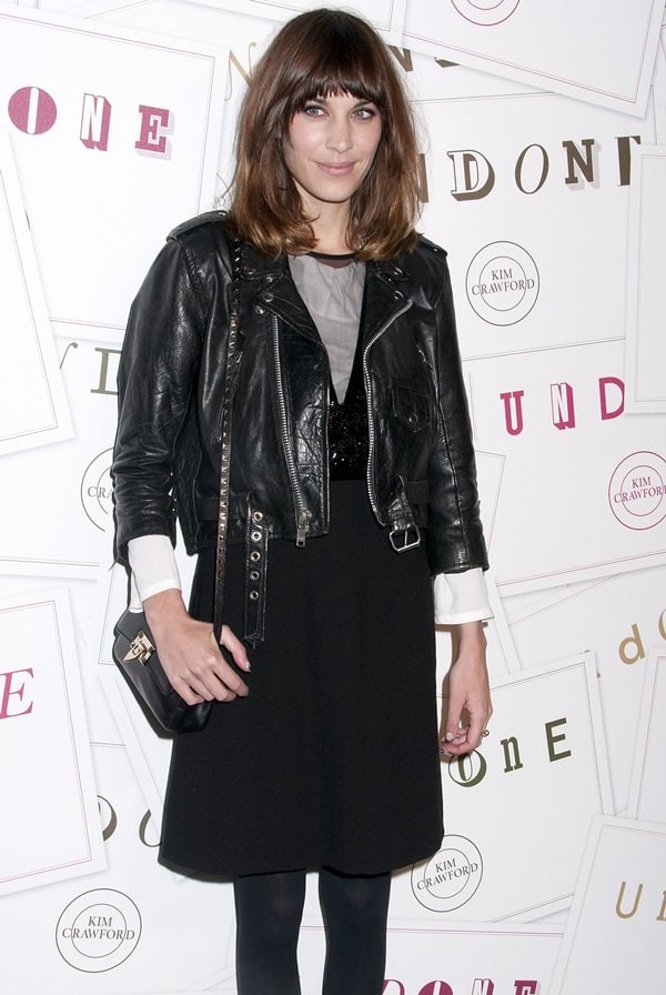 Alexa Chung effortlessly blends edgy and preppy, layering a classic black leather biker jacket over a chic monochrome dress with a crisp white shirt, tights, and a structured crossbody bag