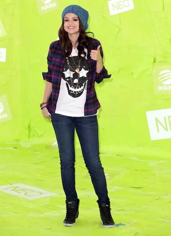 Dressed in Adidas NEO, Selena Gomez combines a white skull shirt, blue jeans, and a checkered shirt-jacket with black kicks at the Los Angeles event