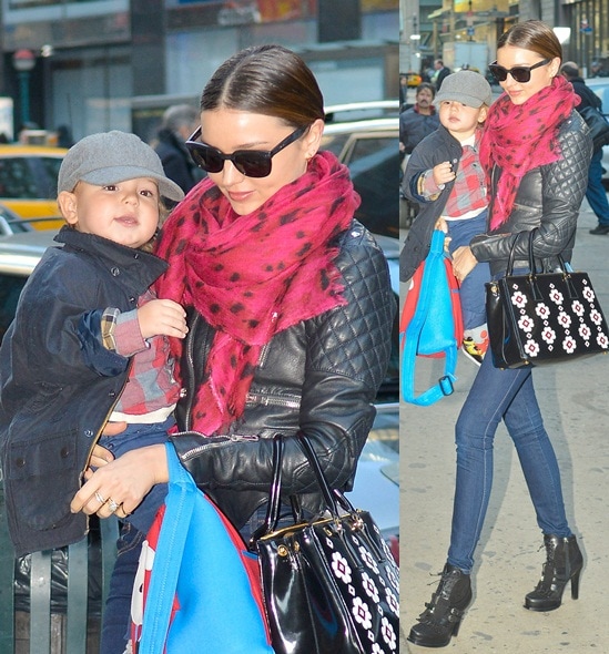 Miranda Kerr nails the biker-chic look in a quilted leather jacket, skinny jeans, and edgy ankle boots while accessorizing with a bold red scarf and a floral Prada tote, carrying her adorable son Flynn in New York City