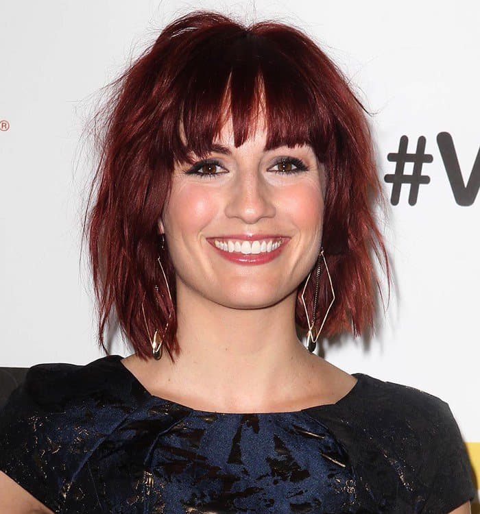Alison Haislip rocks a bold textured red bob with eye-grazing bangs, complemented by a radiant complexion, soft smokey eyes, and a glossy nude lip for a fresh yet edgy vibe