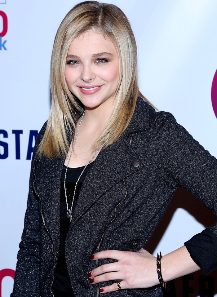 Chloë Grace Moretz pairs her sleek blonde hairstyle with a layered necklace and bold red nails, effortlessly complementing her edgy Aeropostale moto jacket