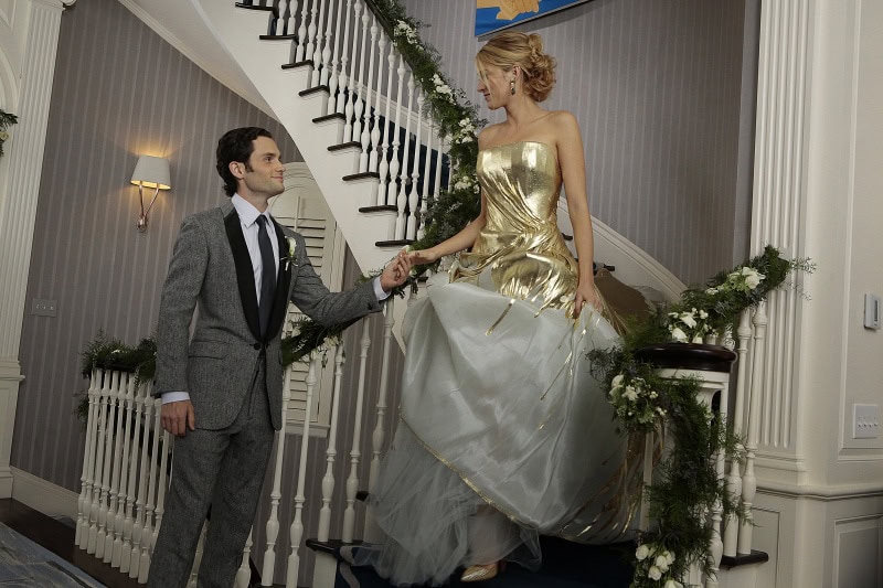 Blake Lively, as Serena van der Woodsen, stuns in a strapless gold-and-white Georges Chakra Couture wedding gown with matching gold heels, beside Penn Badgley’s Dan Humphrey in a sharp gray tuxedo