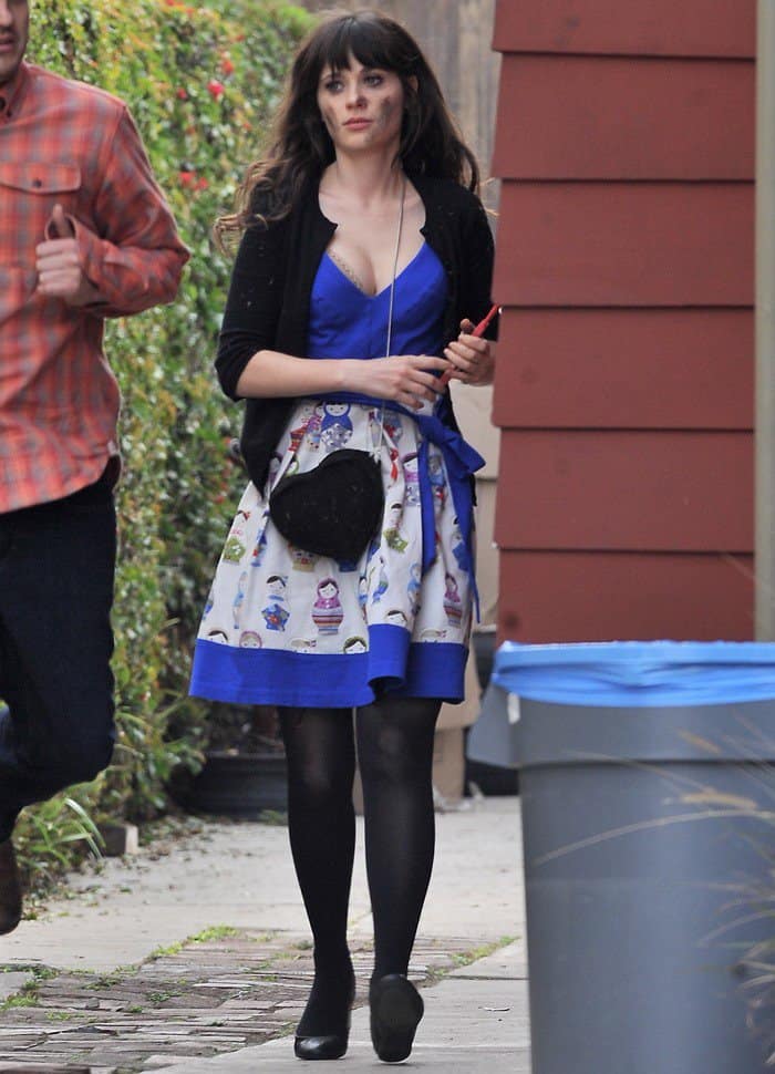 Zooey Deschanel showcases her unmistakable 'adorkable' style on the set of 'New Girl,' featuring her iconic royal blue dress, black cardigan, and enigmatic heart-shaped bag