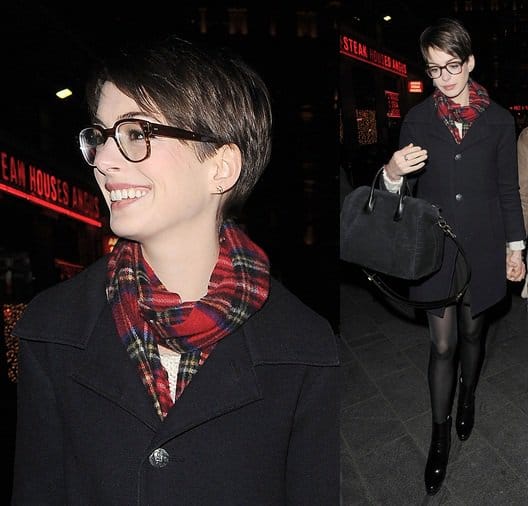 Anne Hathaway wears a scarf, dark-rimmed glasses, a black coat, and booties