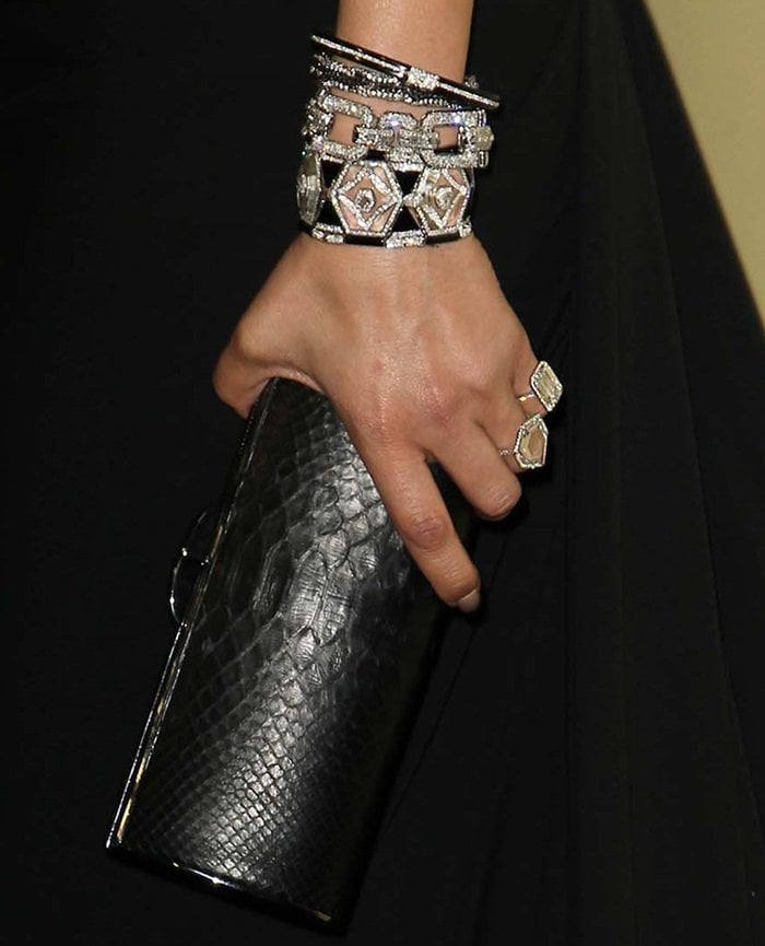 Detailed view of Jennifer Lopez's exotic black snakeskin barrel hardcase clutch paired with her sparkling jewelry