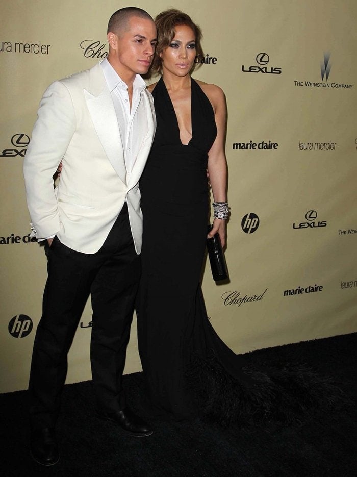 Jennifer Lopez exudes Old Hollywood glamour in a plunging black gown paired with sparkling jewelry, standing alongside Casper Smart in a crisp white tuxedo
