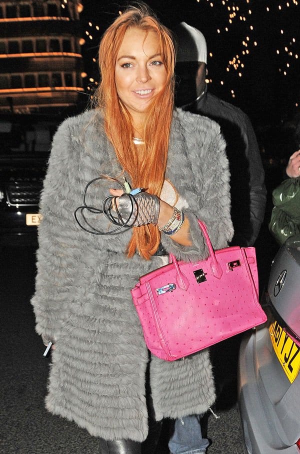 Lindsay Lohan makes a statement on the streets of London, showcasing her impeccable taste with a vibrant pink Hermes Birkin bag, perfectly complementing her urban chic ensemble