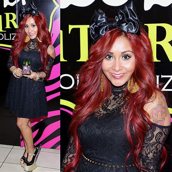 Snooki stuns in a black lace dress, gold statement earrings, a bold satin bow, and her signature heel-less platform shoes at her 'Snooki Couture' fragrance launch