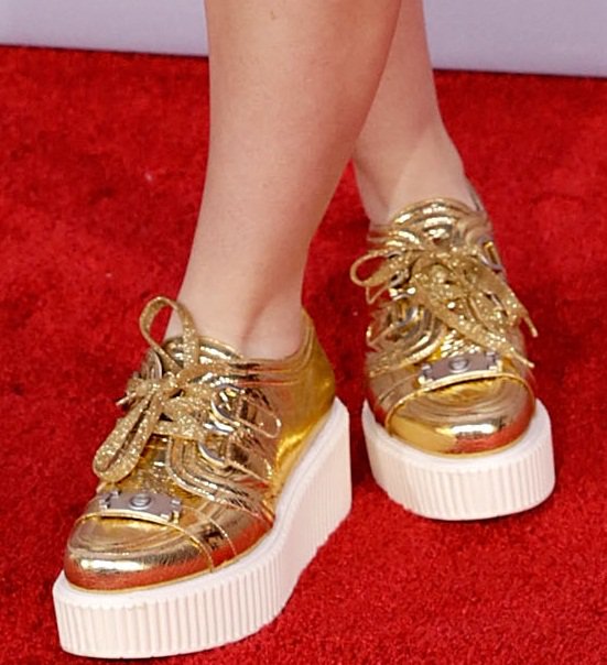 A detailed glimpse into Kathryn Newton's fashion-forward choice: gold flatform Chanel sneakers that redefine red carpet footwear