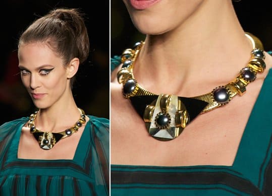 A model wears a neckpiece with an angular pendant and flatback stones set against a round gold choker