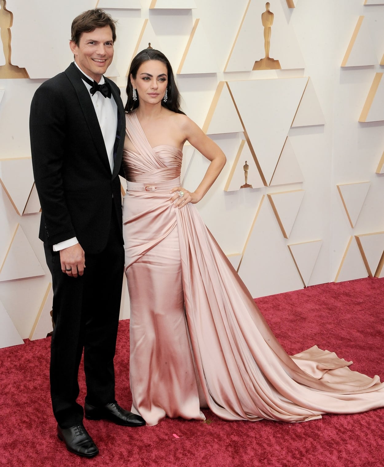 Ashton Kutcher in a black suit and Mila Kunis in a light pink belted Zuhair Murad dress at the 94th Annual Academy Awards