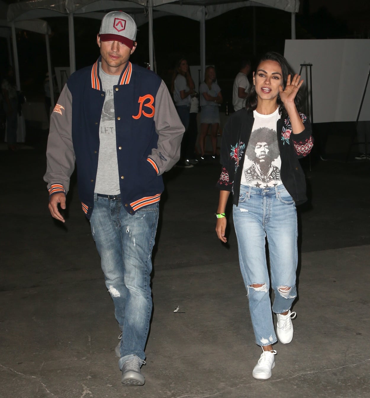 Ashton Kutcher and Mila Kunis in jeans with a Johnny Was Nadia floral bomber jacket, a Lauren Moshi Jimi Hendrix Wolf Foxy Lady tee, and white Vans Authentic sneakers attend the 6th annual PingPong4Purpose