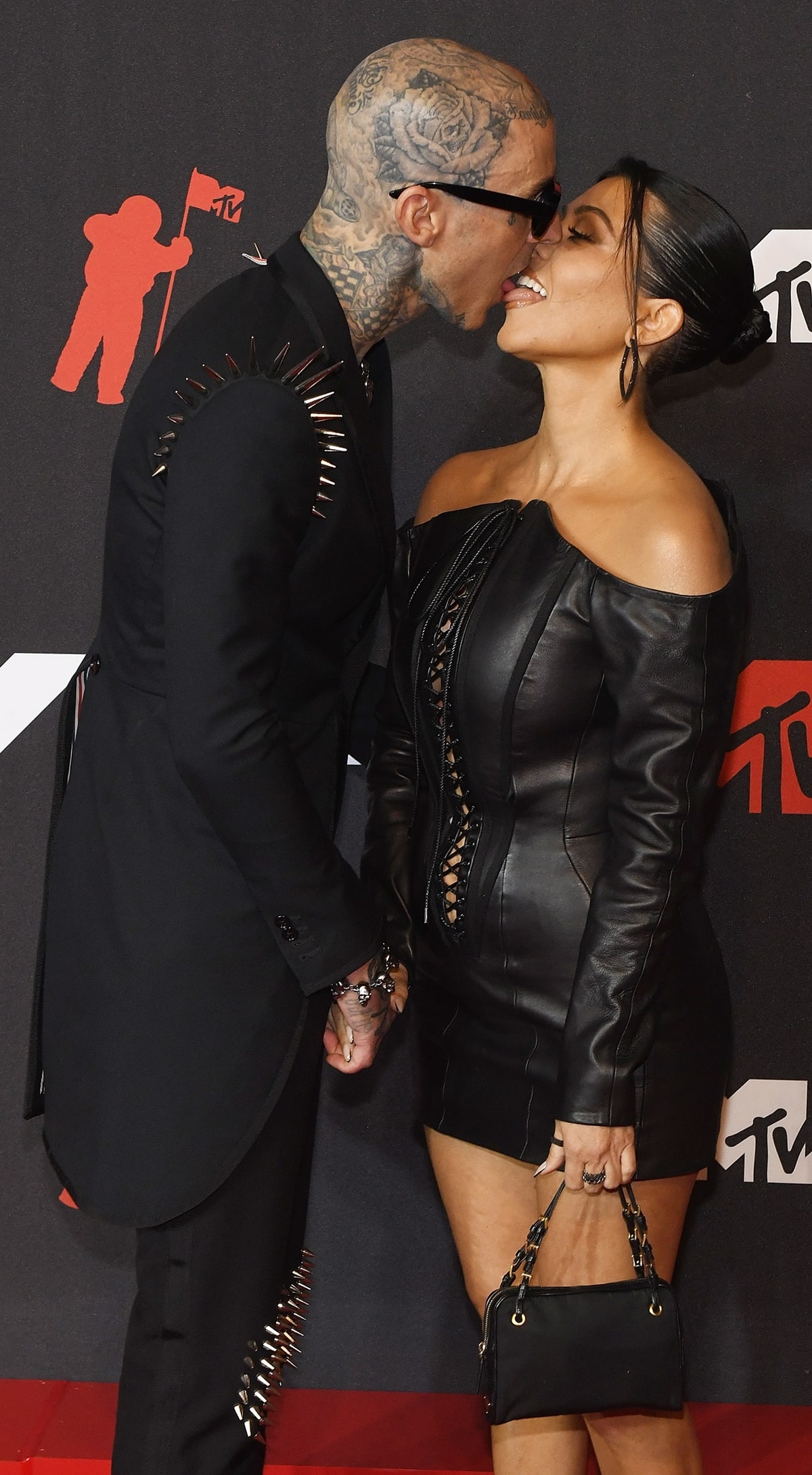 Wearing a black leather dress with long sleeves, Kourtney Kardashian kisses her boyfriend Travis Barker