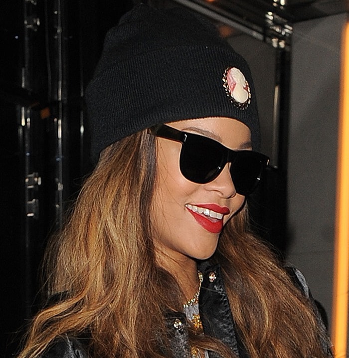 Rihanna styled her loose, honey-blonde waves with a vintage-inspired black beanie featuring a cameo brooch, flashing a bright smile as she left her London hotel