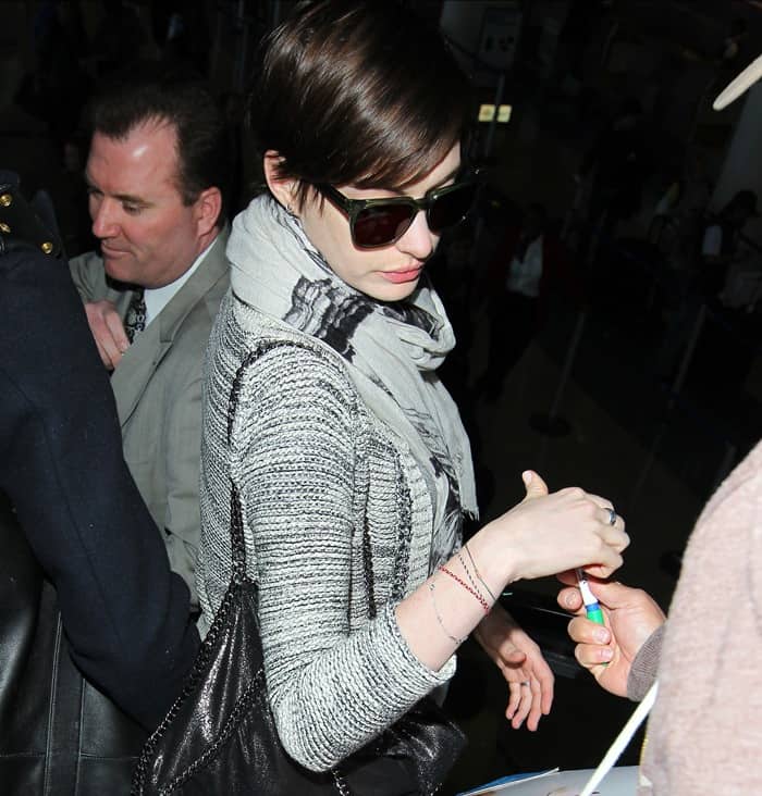Anne Hathaway in a grey knitted cardigan paired with a cream printed scarf draped over her shoulders and a black leather handbag