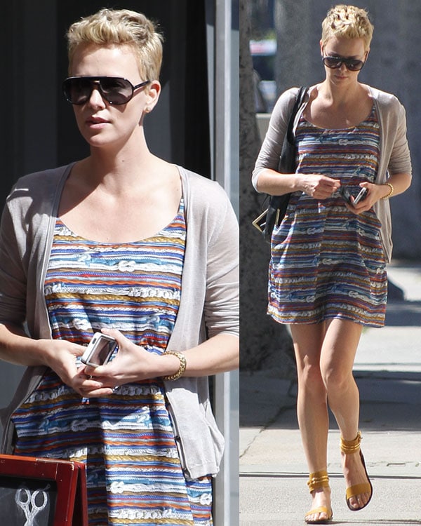 Charlize Theron exudes effortless summer chic in a colorful striped dress, beige cardigan, and bold mustard Maiyet ankle-cuff sandals