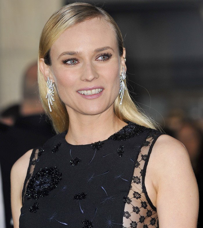 Diane Kruger exudes elegance with sleek, side-parted hair, soft pink makeup, and eye-catching statement earrings