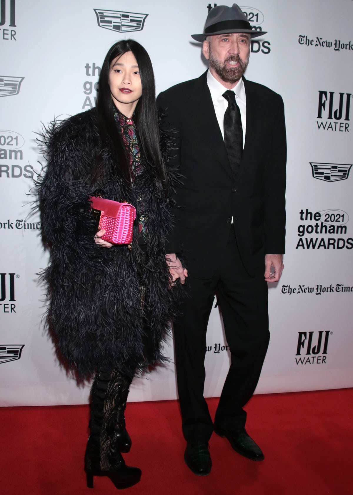 Riko Shibata stuns in a feathered black coat and pointed-toe lace-up boots, while Nicolas Cage complements her look in a classic suit paired with polished green leather shoes