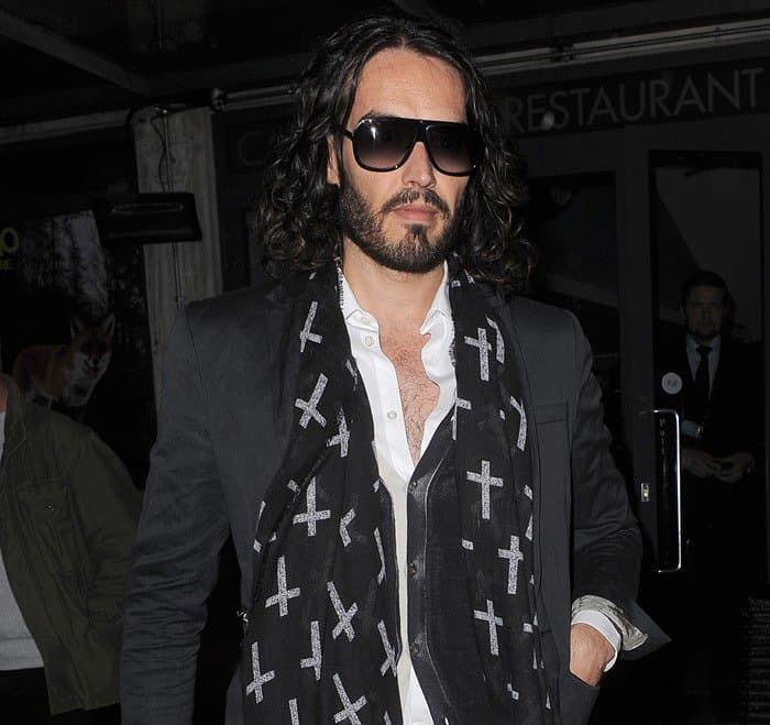 Showcasing effortless style, Russell Brand pairs his eye-catching cross-printed scarf with a crisp white shirt and sleek black jacket, accessorized with classic sunglasses