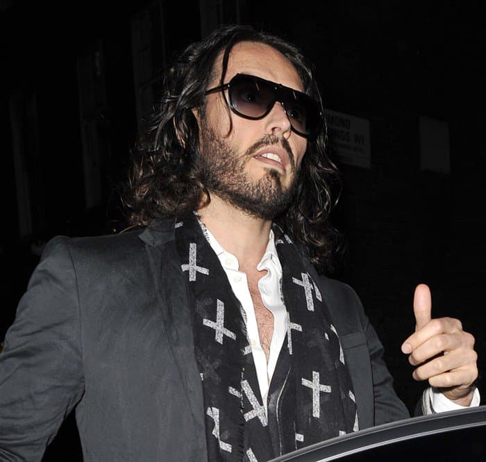 Russell Brand exudes cool charisma as he steps out of the Soho Theatre, donning a statement crucifix-patterned scarf that perfectly complements his outfit