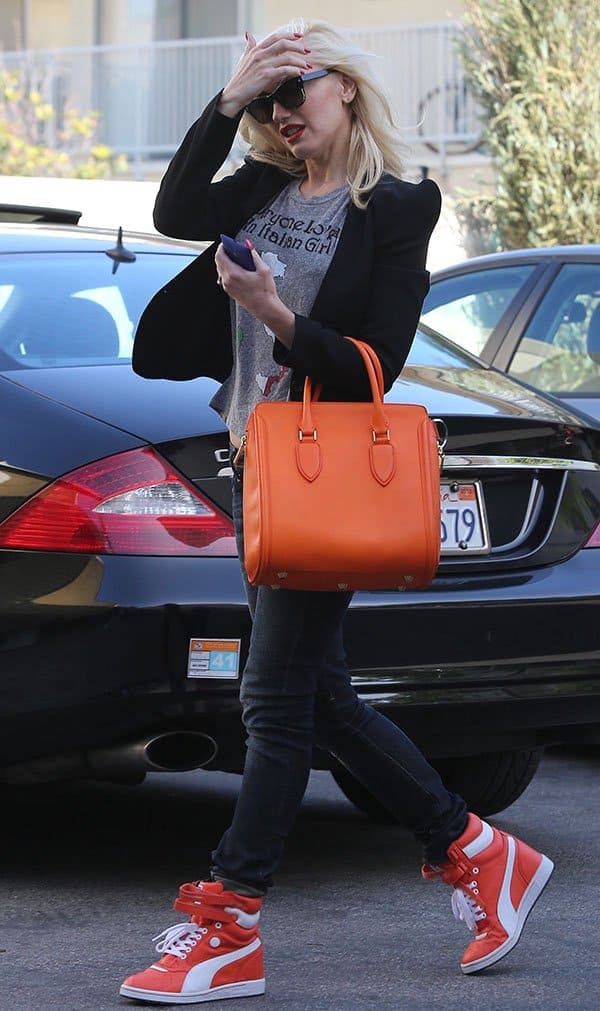 Gwen Stefani carried a vibrant orange Alexander McQueen bag, harmoniously complementing her high-top sneakers