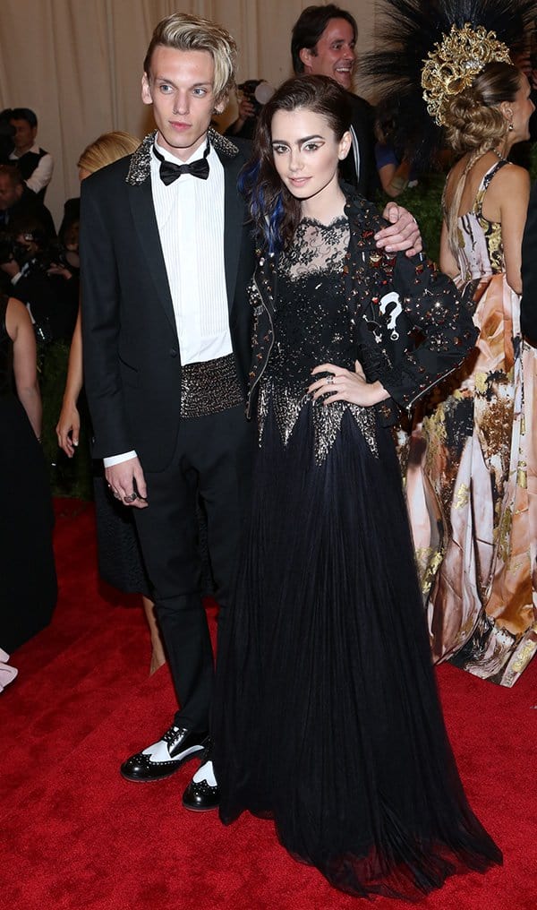 Posing with her boyfriend, Jamie Campbell Bower, Lily Collins embraces her punk side in a black Moschino gown adorned with vintage accents at the Met Gala