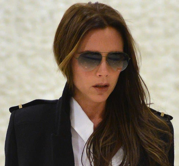 Victoria Beckham in a black trench coat worn over a white button-down top