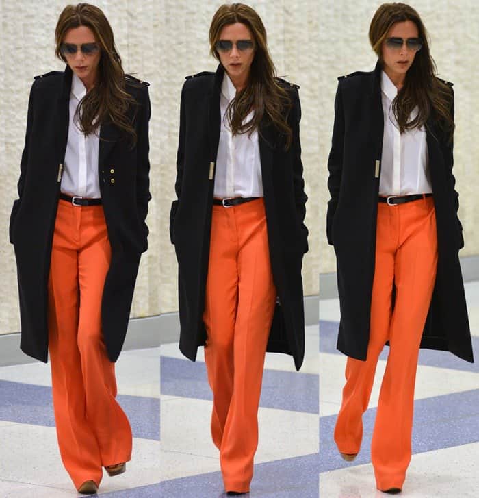 Victoria Beckham spotted at JFK Airport donning vibrant orange flare pants from her own collection, adding a pop of color to her ensemble