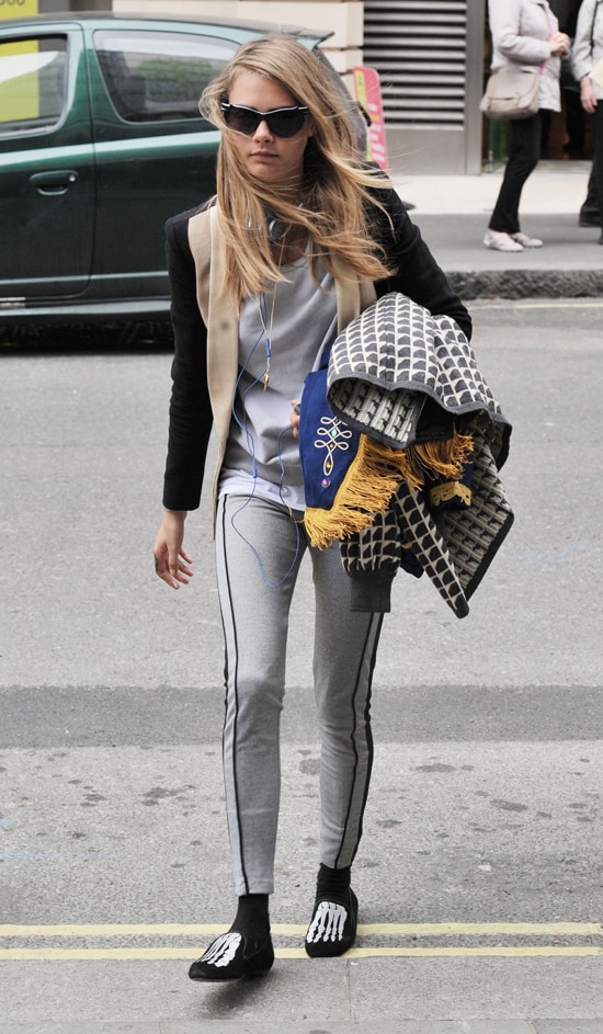 Cara Delevingne exudes casual chic in two-tone leggings, skeleton-print Mara & Mine slippers, and Lulu Guinness sunglasses, layering effortlessly for a bold street style