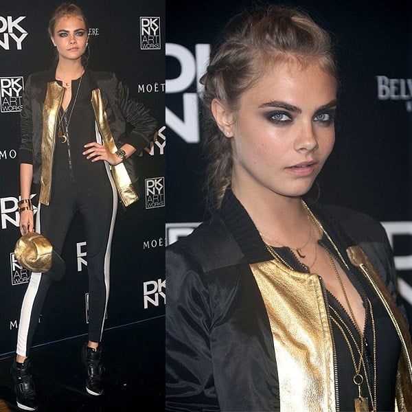 Cara Delevingne in a striped jumpsuit, a gold-trimmed varsity jacket, a gold snapback cap, and the DKNY "Pulse" booties
