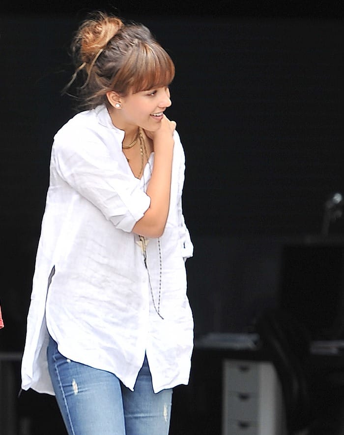 Jessica Alba is captured in a candid moment, her laughter adding a lively spark to the casual elegance of a classic white shirt and distressed blue jeans ensemble