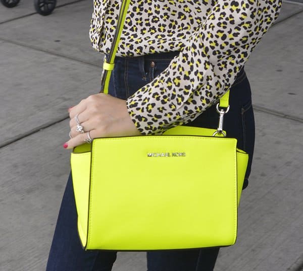 Miranda Kerr accentuates her travel attire with a striking neon yellow Michael Kors 'Selma' messenger bag, adding a vibrant touch to her sophisticated ensemble