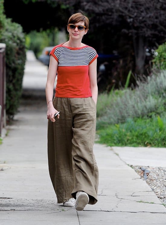Anne Hathaway's outfit consists of wide-legged, baggy pants paired with a baby T-shirt, a style choice that has been criticized for not being flattering