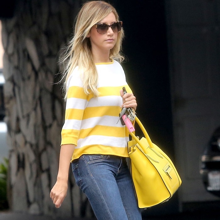 Ashley Tisdale rocks a casual chic look with a yellow and white striped sweater, blue jeans, and accessorizes with a yellow Celine Boston Bag and aviator sunglasses