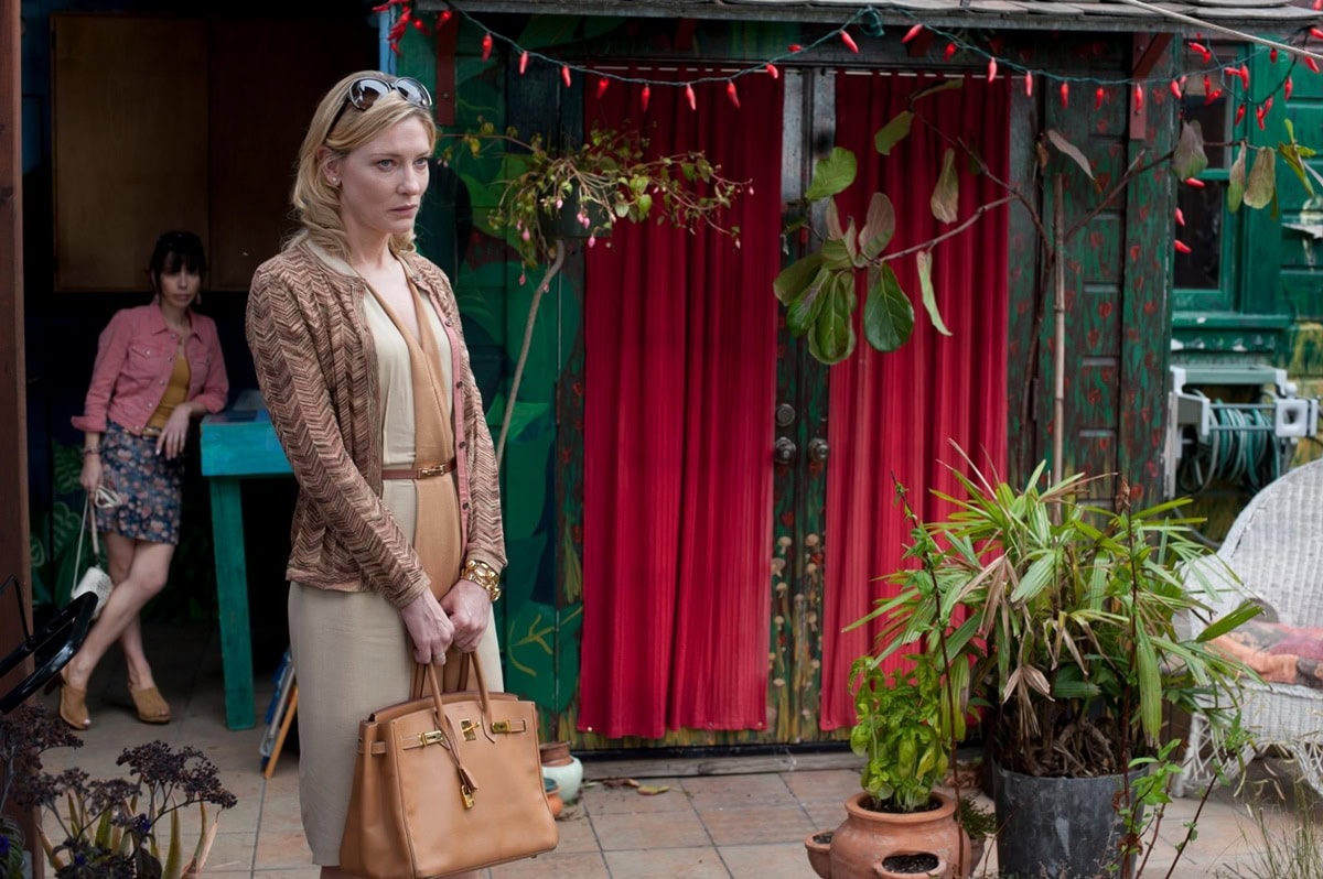 Cate Blanchett as Jasmine in Blue Jasmine exudes upscale elegance in a belted beige dress, textured cardigan, gold cuff, and a coveted tan Hermès Birkin bag
