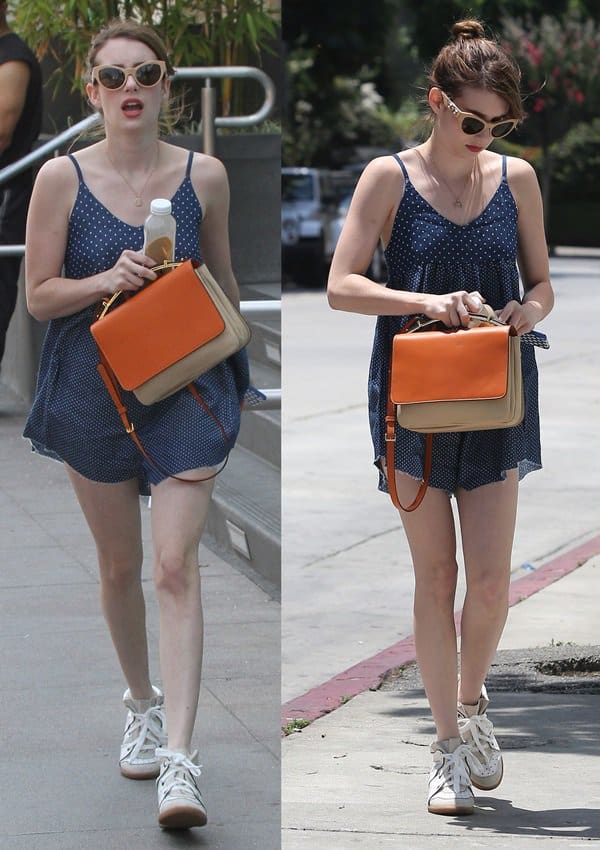 Emma Roberts accessorized with a pair of wedge sneakers, huge sunglasses, and an orange handbag that provided a complementing contrast to her blue romper