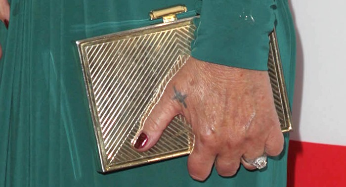 Helen Mirren adds a touch of sophistication with a chic gold clutch, while her deep burgundy manicure complements her elegant look perfectly