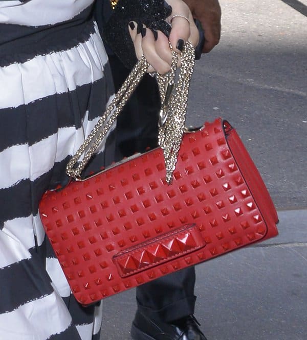 Kris Jenner elegantly holds a striking Valentino Rock Stud Chain Flap Bag in Rogue, adding a luxurious touch to her outfit