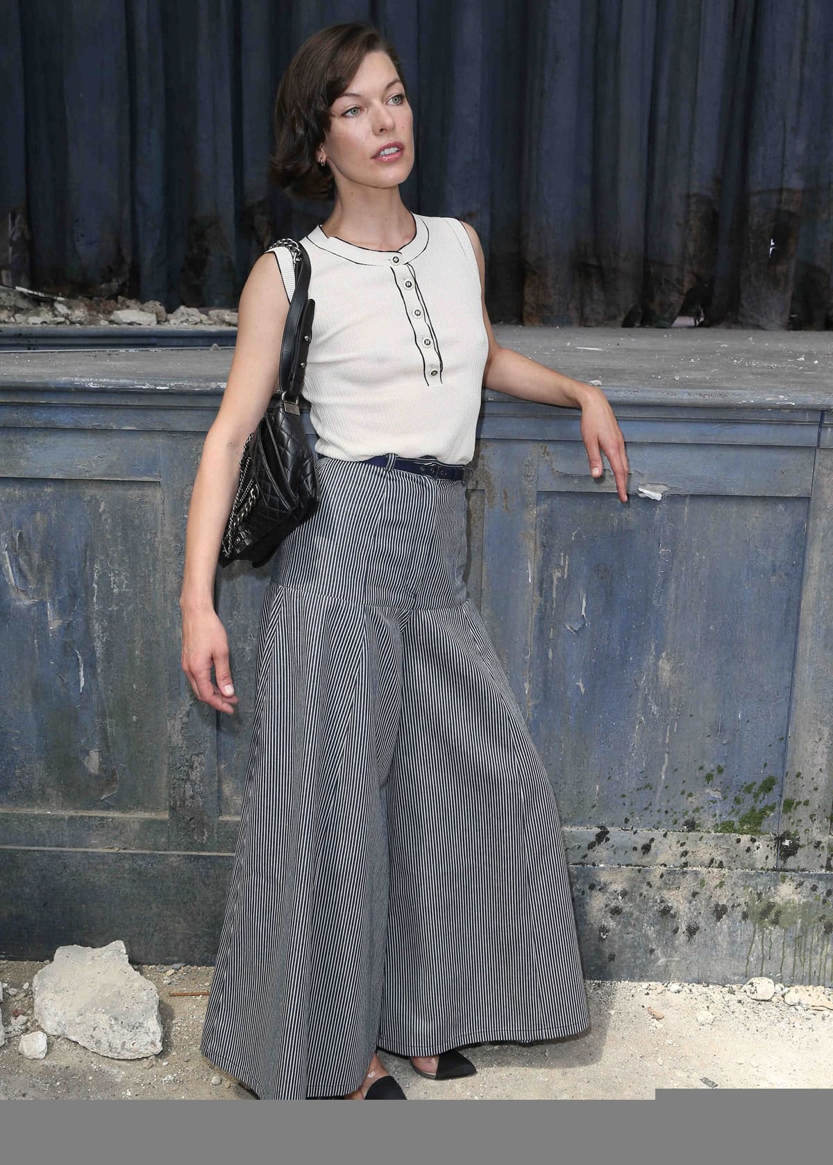 Milla Jovovich exudes classic chic in pinstripe wide-leg trousers and a buttoned blouse as she elegantly poses at the Chanel Haute-Couture show during the Paris Fashion Week Fall/Winter 2013-2014 at the Grand Palais in Paris