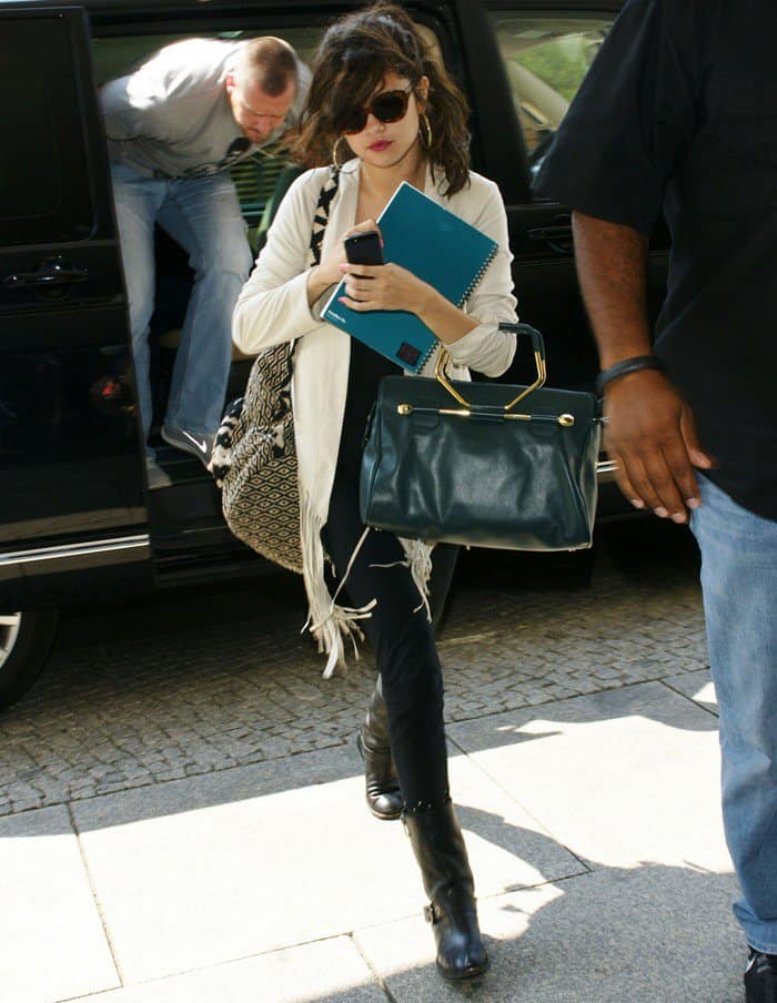 Selena Gomez makes a stylish entrance at Berlin's Grand Hyatt, dressed in Vince Camuto boots and Adidas leggings, complemented by her cream Sw3 fringe jacket and designer accessories, on July 8, 2013