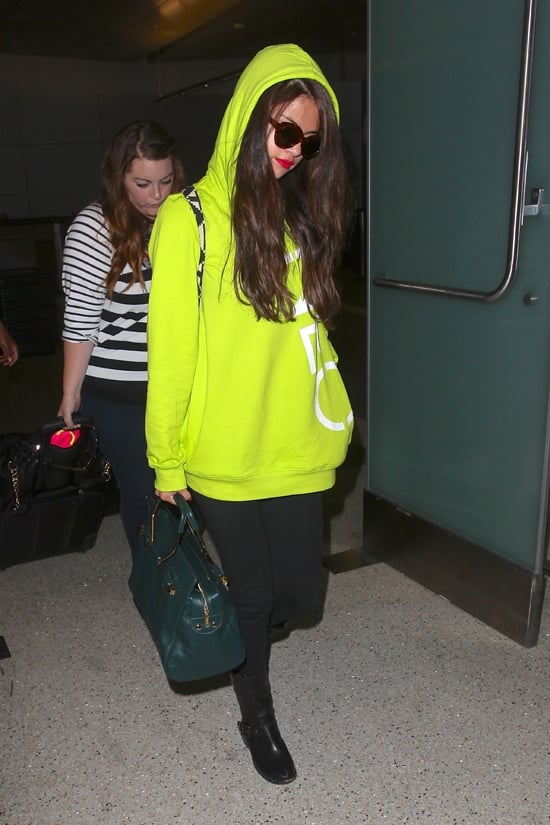 On July 10, 2013, at LAX Airport, Selena Gomez was spotted wearing Vince Camuto Walt Stud boots, Viktor & Rolf Bombette bag, Adidas Neo Selena Gomez leggings, a lime Adidas Neo logo hooded sweatshirt, and Elizabeth and James Taylor cat eye sunglasses