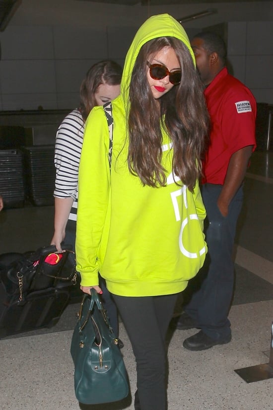 Selena Gomez captivates in a vibrant neon Adidas Neo hoodie paired with chic accessories, showcasing her unique style at LAX after her Europe trip, July 10, 2013