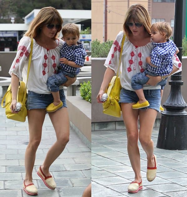 Selma Blair effortlessly balances motherhood and style during a leisurely outing, cradling her son while donning her beloved Siwy Jeans 'Camilla' cutoff shorts, complemented by vibrant yellow accessories that add a pop of color to her chic, comfortable ensemble