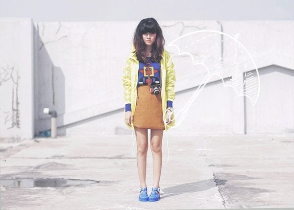 Sonia rocks a bold and eclectic look with a vibrant yellow raincoat, quirky robot-print top, vintage-style pencil skirt, and bright blue jelly sandals for a playful retro vibe