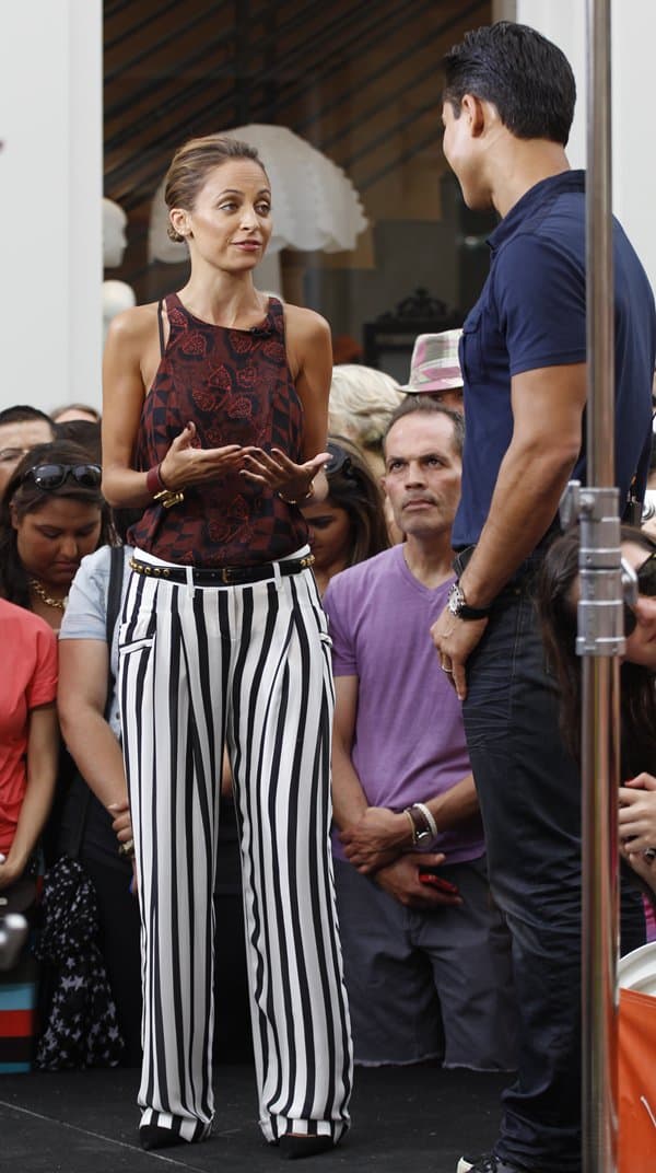 Nicole Richie engages in conversation on the set of "Extra" at The Grove in Los Angeles on July 10, 2013, wearing an ensemble that includes striped Balmain silk georgette pants and a blood floral A.L.C. Huntley blouse, accented with a Saint Laurent skinny studded belt