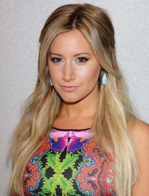 Ashley Tisdale radiates elegance with her voluminous half-up, half-down hairstyle, turquoise teardrop earrings, and a bold, kaleidoscopic Clover Canyon dress featuring intricate paisley and botanical prints