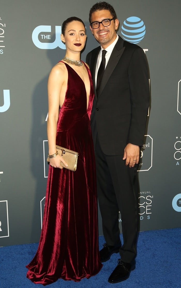 Emmy Rossum radiates sophistication in a deep burgundy velvet Ralph Lauren gown, accessorized with Fred Leighton jewelry and a gold clutch, as she attends the 2019 Critics’ Choice Awards with her husband, Sam Esmail