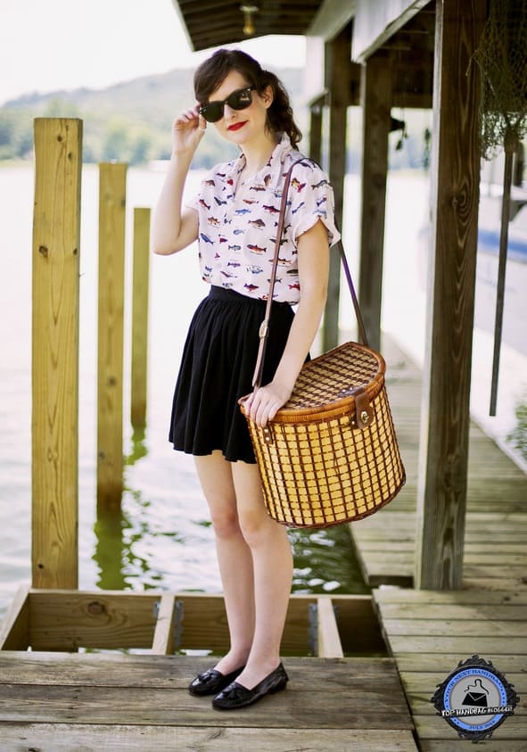 Ashlyn pairs her whimsical fish-print blouse and pleated black skirt with classic loafers and a charming picnic basket handbag for a retro-chic lakeside look