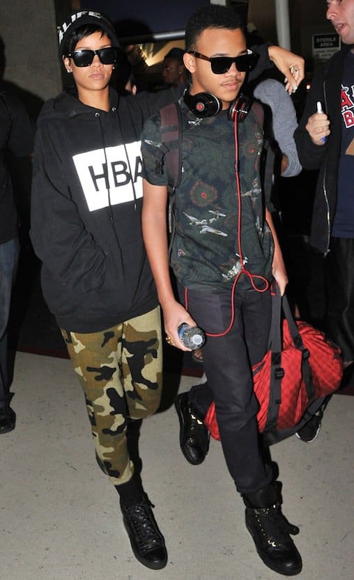 Rihanna arriving at Los Angeles International Airport with her younger brother Rajad on August 27, 2013, effortlessly showcasing her hip-hop style in a Hood by Air hoodie and camo sweatpants